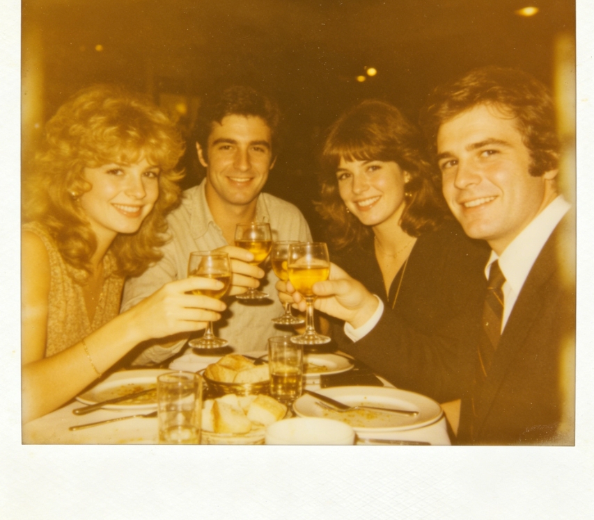 1970s Polaroid instant photo, white border, yellowed faded tone, heavy grain, casual dinner gathering, centered composition