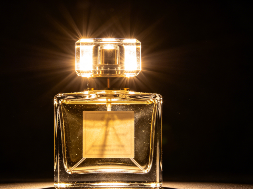 Product photo of perfume bottle with clear glass, warm studio light on black background, strong light reflections on bottle and cap blurring label details, original image for AI glare removal