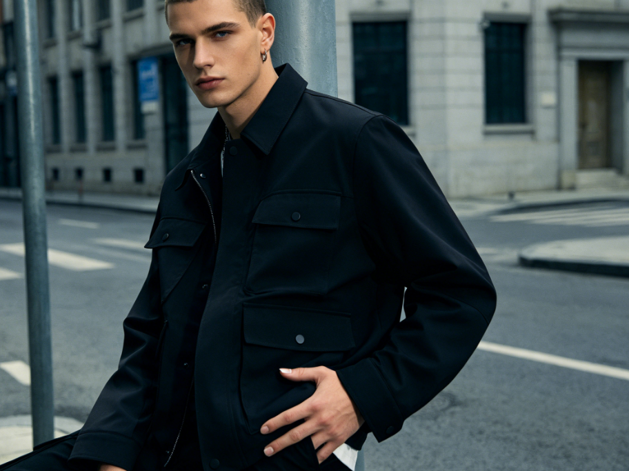Bust portrait of a European man in a street fashion shoot, neat short hair, black workwear jacket, one hand in pocket, hands naturally visible, nails in natural nude color, 4:3 aspect ratio portrait photography