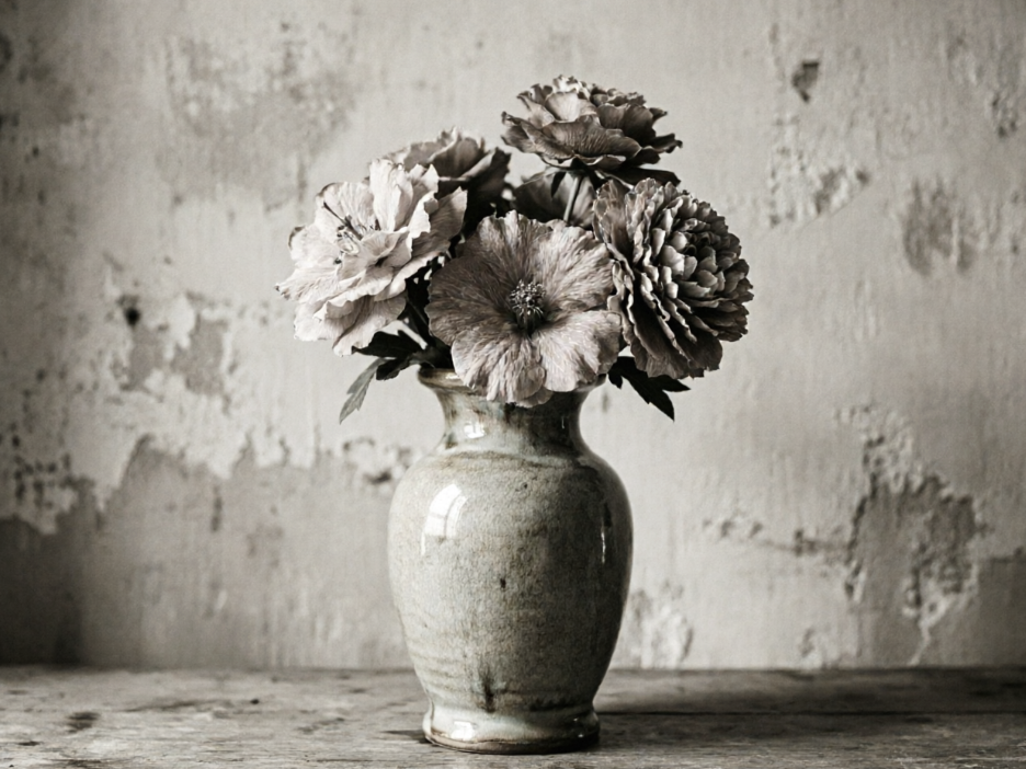 Still life photo of a ceramic vase with flowers, vintage mottled wall and wooden table background, low-saturation gray-toned flowers and weathered vase, overall artistic retro style, 4:3 aspect ratio