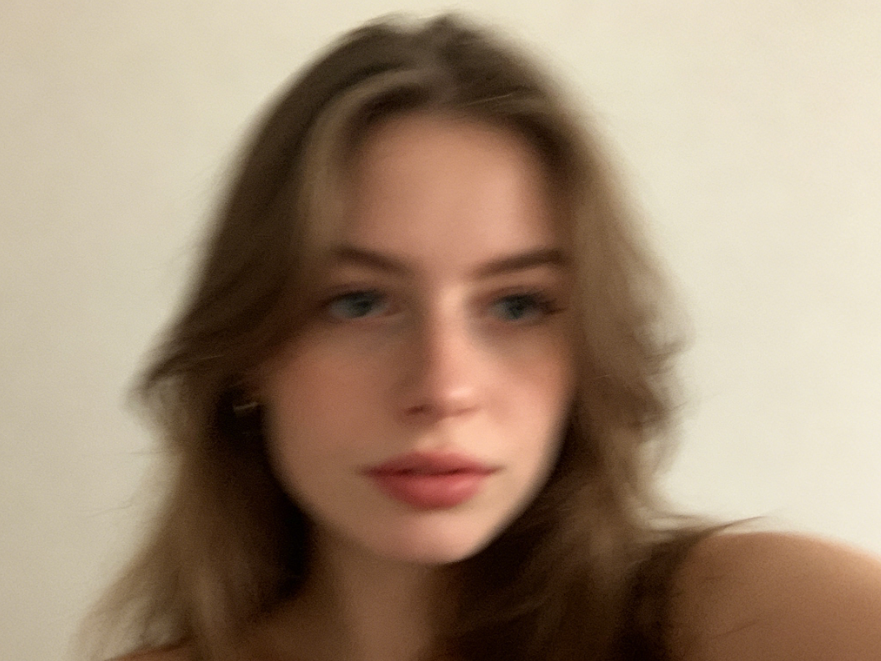 Blurry Caucasian selfie with soft indoor lighting, plain background, overall out-of-focus effect, unclear details, low resolution, no post-processing