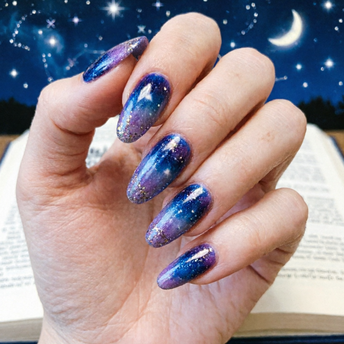 Blue-to-purple gradient nails with gold glitter and white stars; night sky and open book background evoke cosmic fantasy.