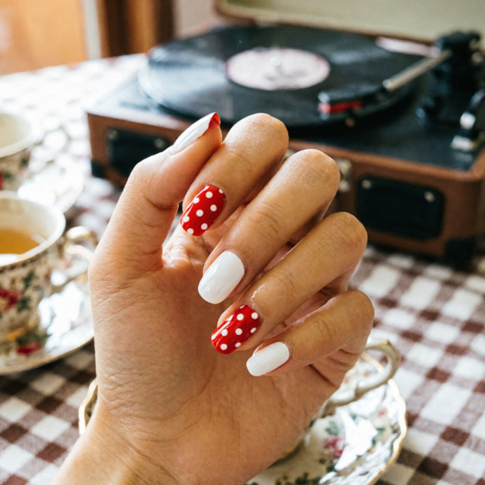 Red polka-dot and solid white alternating nails beside vintage record player and teacup; checkered tablecloth evokes nostalgic tea-time charm.