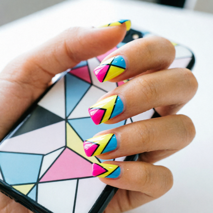 Hand on sketchbook; nails in pure white with black geometric shapes like squares, triangles, and arrows; pencils and sketches in background reflect modern minimalist artistry.