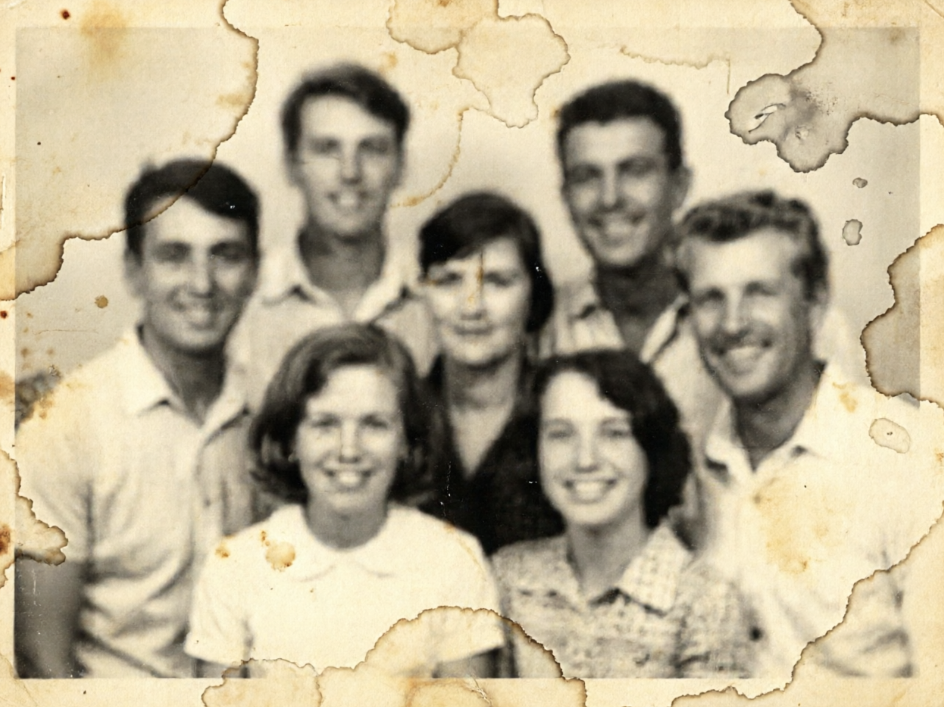 The same group photo rendered with a heavily faded and blurry vintage texture. The image has a sepia tone with lost details, making faces indistinct. There are visible water stains and yellowing damage along the edges of the photo.