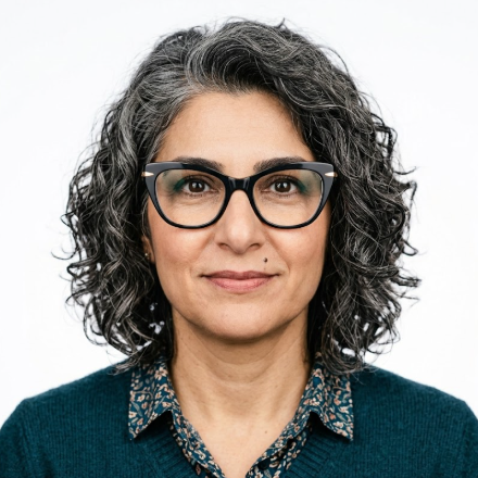 A middle-aged woman with black-rimmed glasses and wavy gray-black hair smiles gently, wearing a dark green cardigan over a patterned blouse. Against a clean white background, she exudes an intellectual and elegant aura.