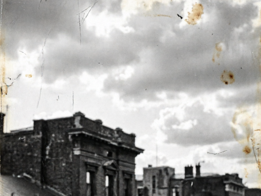  The same scene converted to a low-contrast black and white image. The picture appears hazy and gray, as if covered in dust, with added scratches and stain noise in the sky, mimicking the rough texture of early photography.