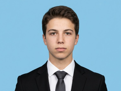 Frontal portrait of the same man with neat hair, now in a black suit, white shirt, and dark tie. His expression is serious and focused against a solid light blue backdrop — standard professional ID photo format.
