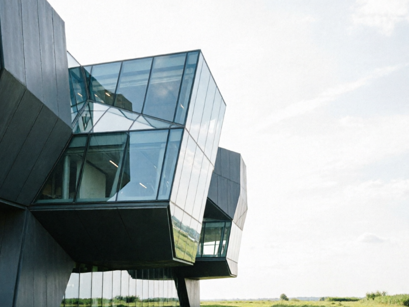 A high-contrast image, with the left side showing a clear photo of an urban landmark building (e.g., an asymmetrical modern art museum), with its unique glass and steel structure leaning towards the left side of the frame, and a portion of clear blue sky and a green area on the right; the right side shows the effect of the same photo after applying a horizontal mirror invert filter