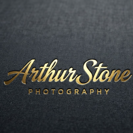 A 1:1 square mockup of a professional signature logo. The name "Arthur Stone" in a sophisticated, sharp-edged script font. The logo is rendered in reflective gold foil embossed onto a dark charcoal grey linen background. Below the signature, the word "PHOTOGRAPHY" is written in a clean, spaced-out sans-serif font.