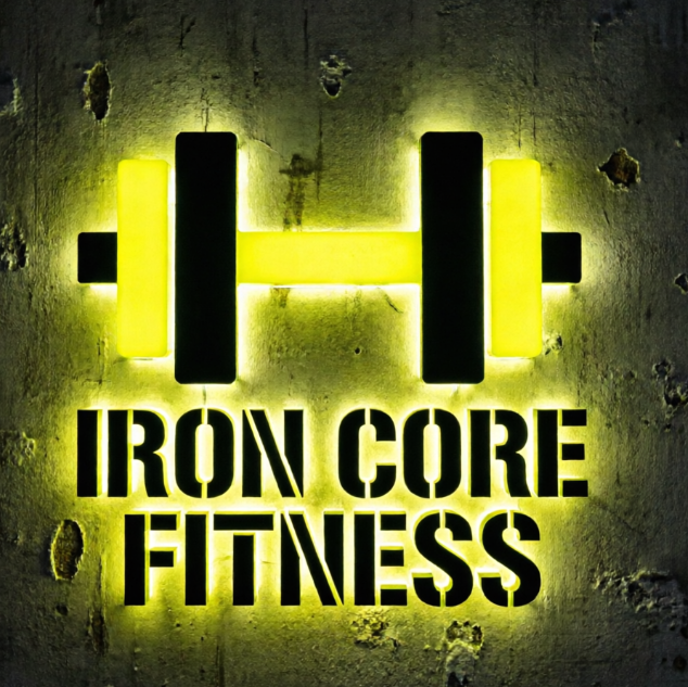 A 1:1 powerful gym logo. A silhouette of a heavy dumbbell formed by clean geometric shapes. High contrast black and fluorescent yellow. Bold, thick sans-serif font reads "IRON CORE FITNESS". The logo is displayed as a backlit 3D sign on a dark industrial gym wall.