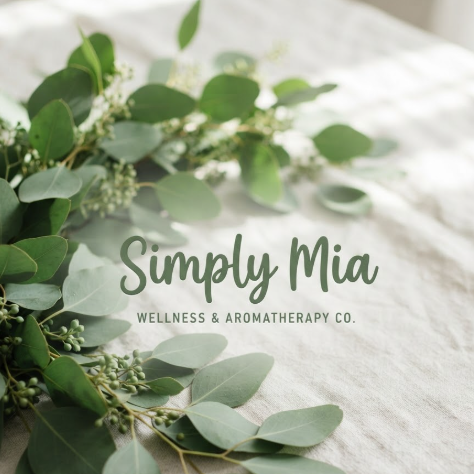 A 1:1 lifestyle branding image. The name "Simply Mia" in a relaxed, legible handwriting style. The logo is in sage green color, centered on a background of fresh eucalyptus leaves and white linen. The lighting is bright and natural, suggesting a healthy, balanced life.