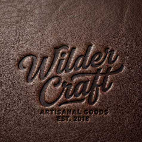 A 1:1 rugged artisan logo. The signature "Wilder Craft" heat-stamped into deep brown, premium pebbled leather. The stamping is deep and shows the realistic texture of the leather grain. The font is a sturdy yet artistic script. The scene feels high-end and durable.