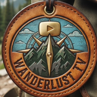 A 1:1 adventure YouTube logo. A circular design featuring a mountain peak silhouette where the summit is a golden play button. A compass needle points towards the center. Earthy tones of forest green and sky blue. "WANDERLUST TV" in rugged, vintage font. Logo printed on a leather luggage tag attached to a backpack.